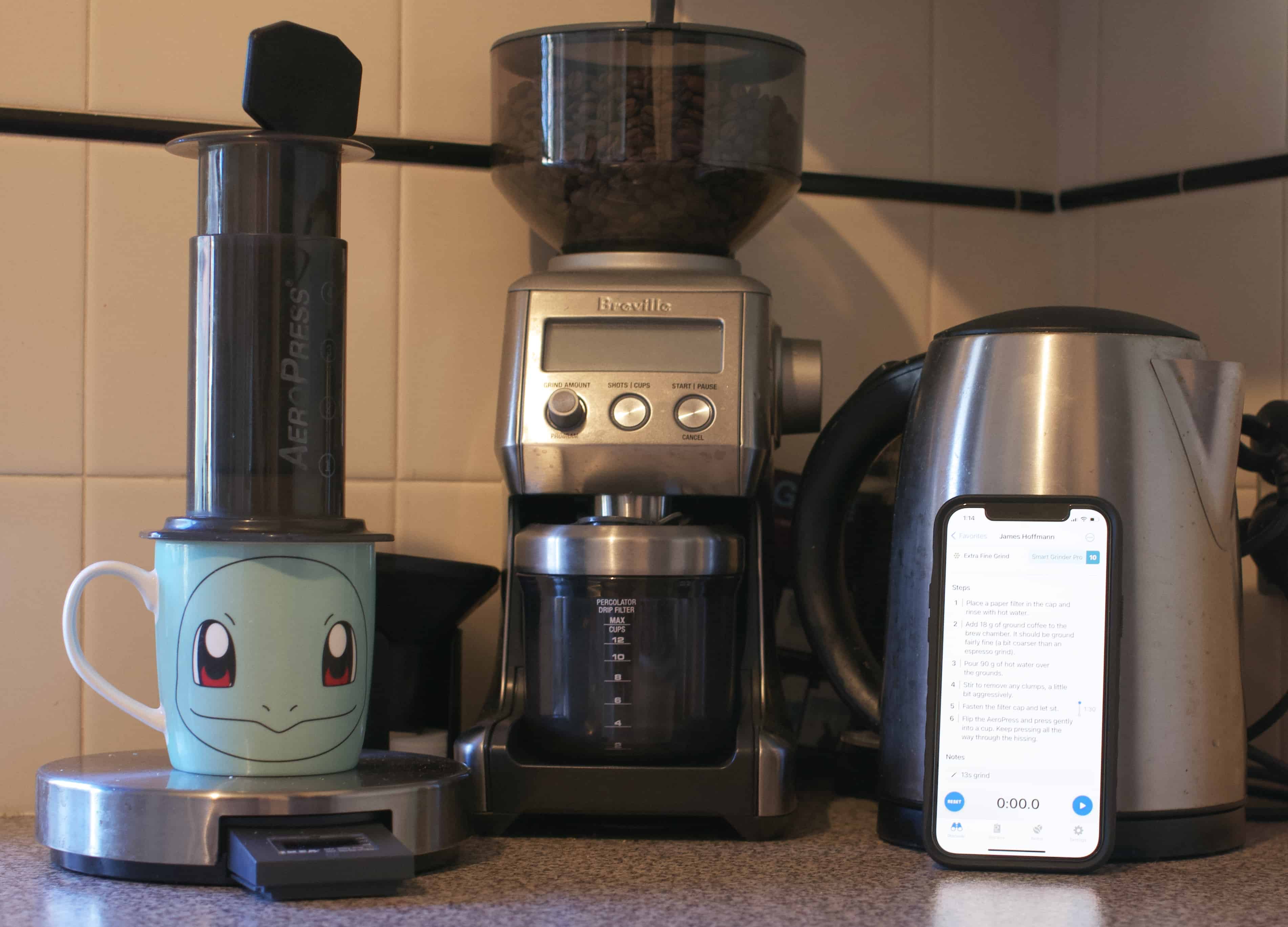 A kitchen counter with a kettle, Aeropress, grinder and a coffee mug